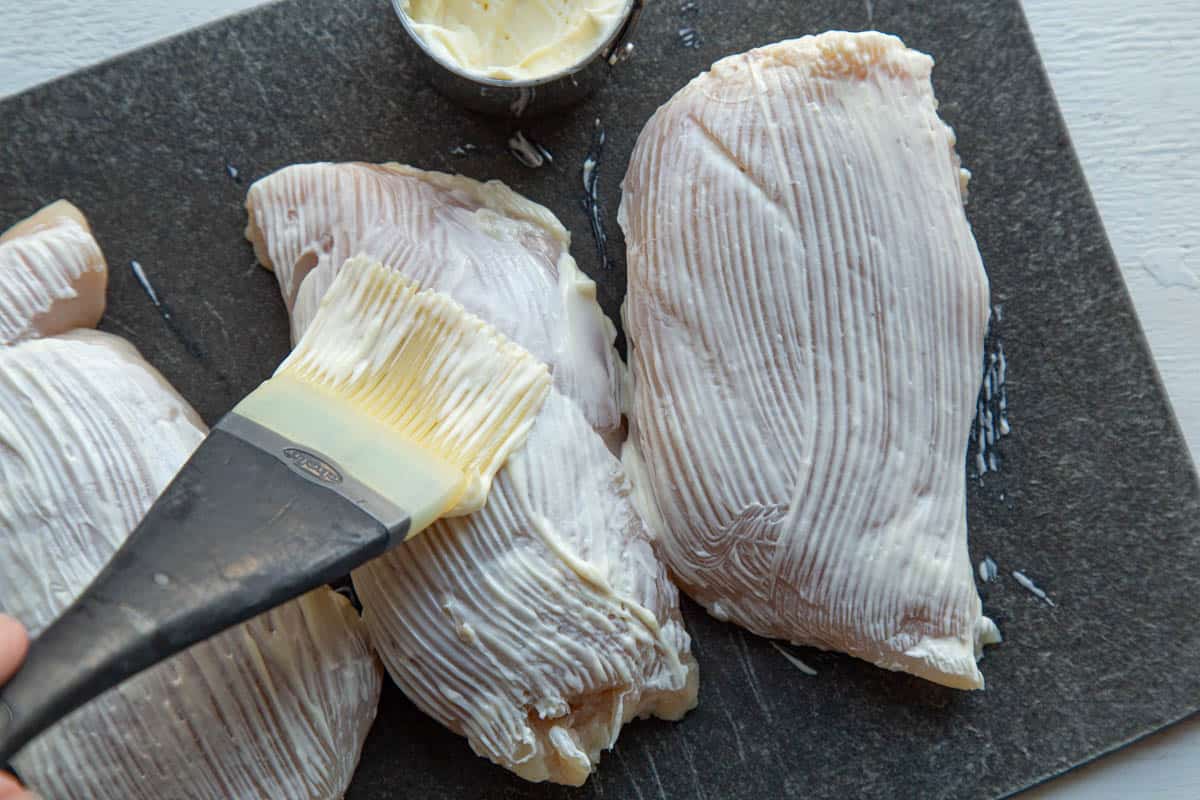brushing chicken breasts with mayonnaise using a pastry brush.