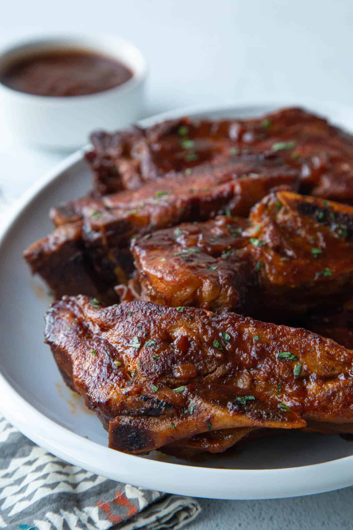 bone-in country style ribs on a white platter with a small bowl of bbq sauce.