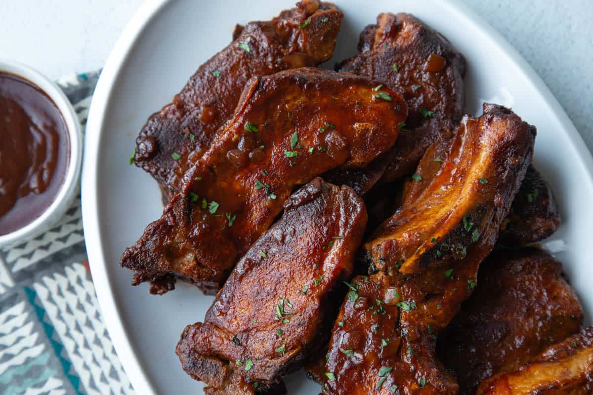 pile of country style ribs with bbq sauce on a white platter.