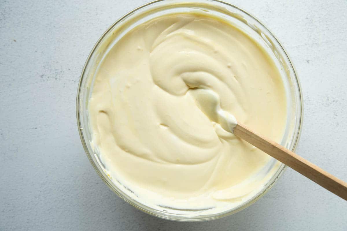 vanilla pudding mixture in a glass bowl with a spatula.