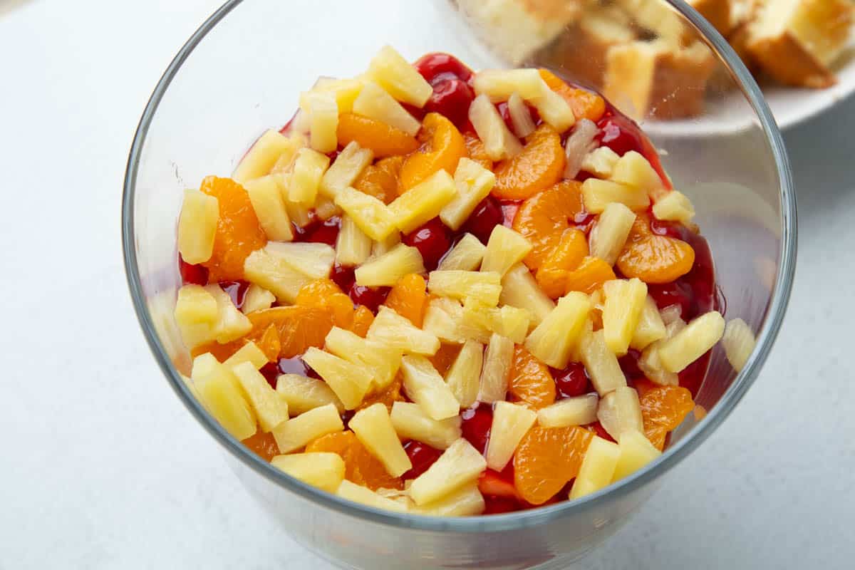 mandarin oranges, pineapple, and cherry pie filling in a glass trifle dish.