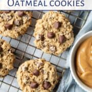 peanut butter oatmeal cookies with chocolate chips on a wire rack next to a small dish of peanut butter.