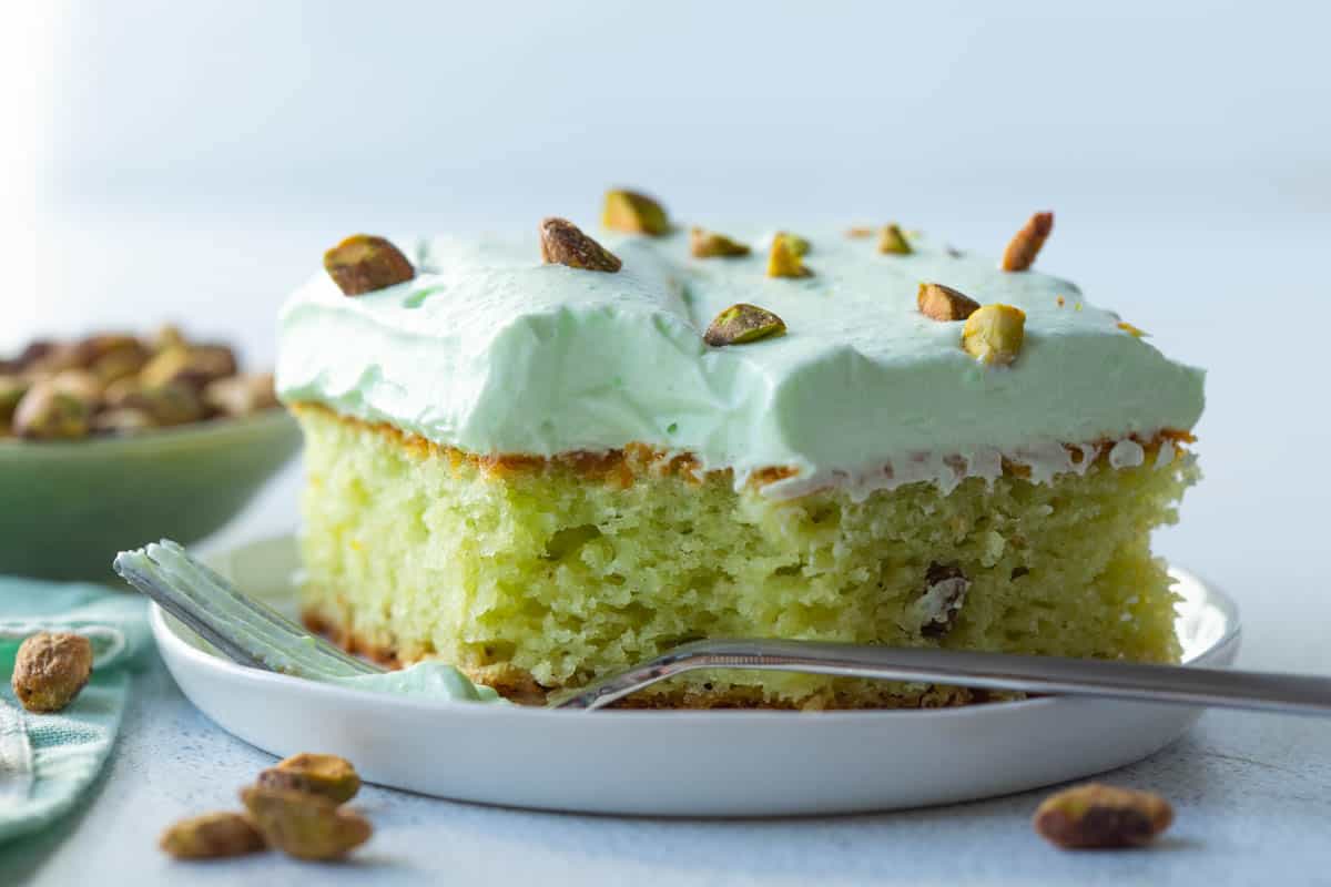 slice of pistachio cake with a bite taken out, sitting on a white plate.