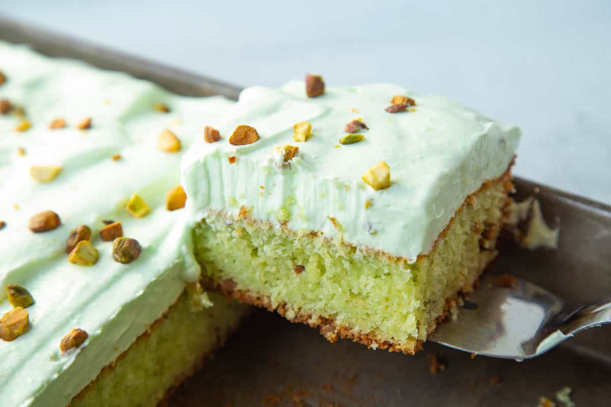 metal spatula lifting a slice of pistachio cake out of a metal pan.