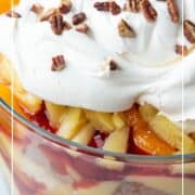 punch bowl cake layered in a glass trifle dish and topped with whipped cream and pecans.