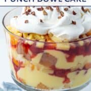 glass trifle dish filled with layers of cake cubes, vanilla pudding, cherry pie filling, and fruit, topped with whipped topping and pecans.
