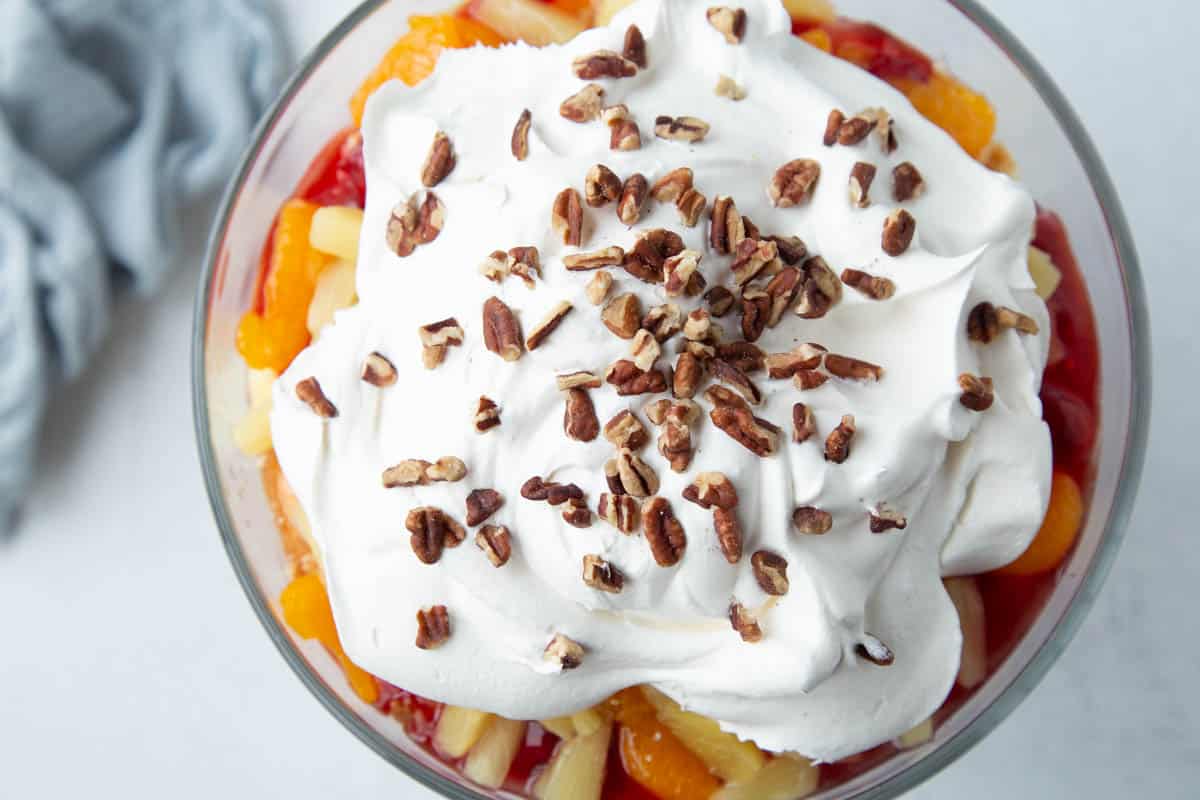 punch bowl cake in a glass dish, topped with whipped cream and chopped pecans.