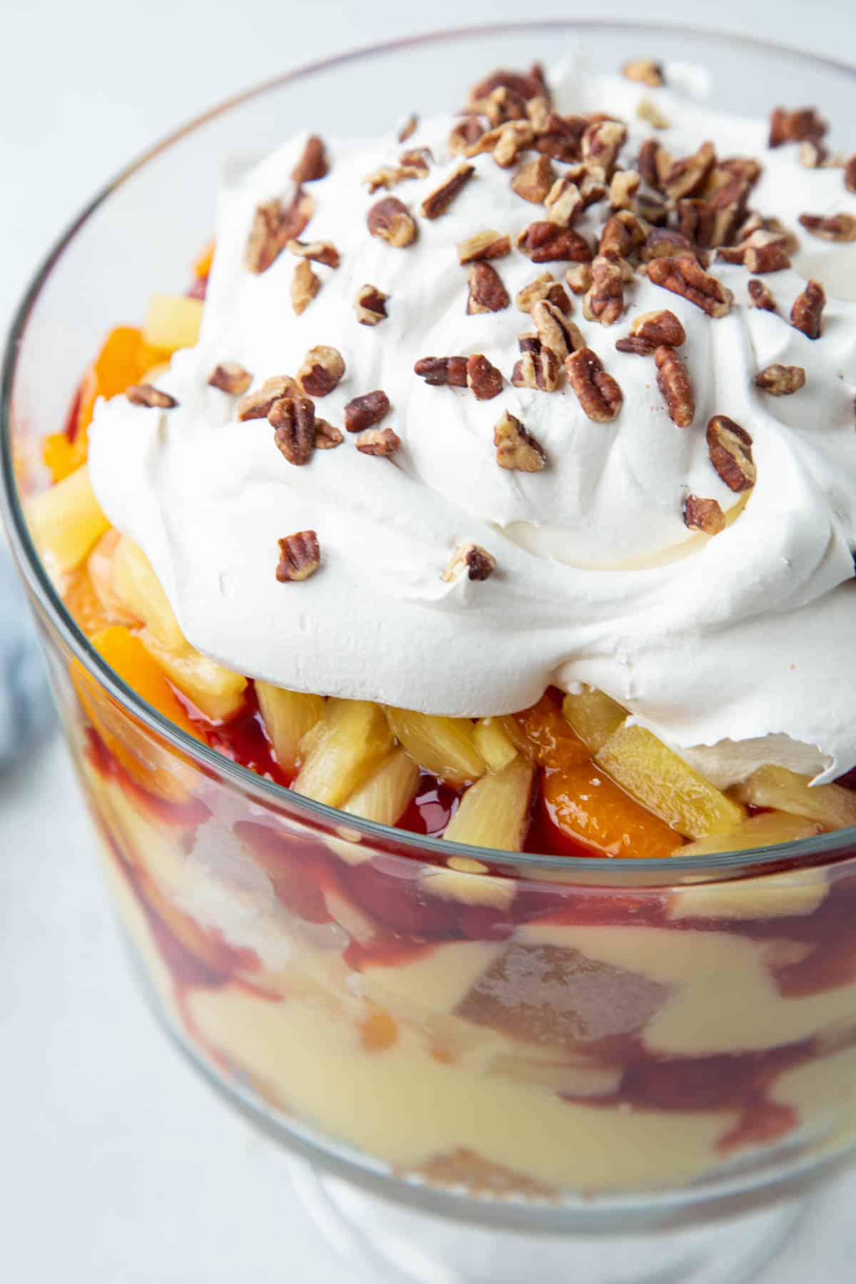 punch bowl cake layered in a glass trifle dish and topped with whipped cream and pecans.