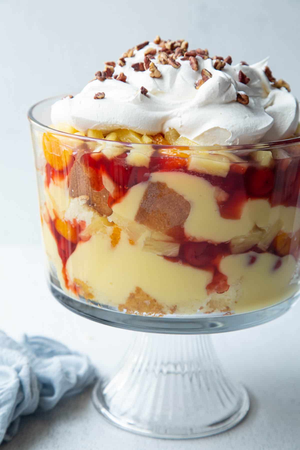 punch bowl cake assembled in a trifle dish with cake, pudding, pie filling, fruit, and whipped cream.
