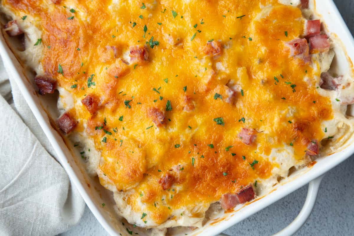 cheese topped scalloped potatoes in a white casserole dish. 