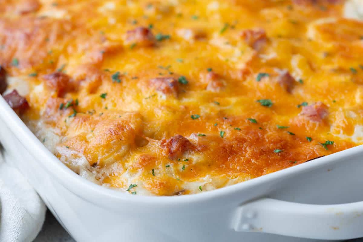 white casserole dish filled with scalloped potatoes and ham, topped with melted cheese.