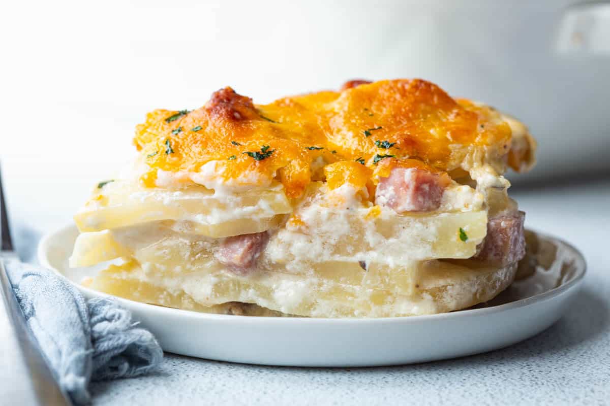 slice of scalloped potatoes and ham topped with melted cheese on a small white plate.