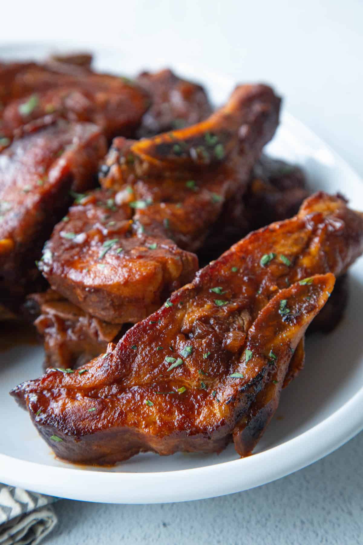 bone-in country style ribs coated in bbq sauce on a white platter.