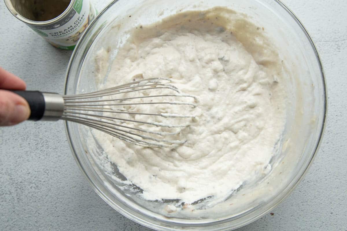 cream of mushroom soup and sour cream in a glass bowl with a whisk.