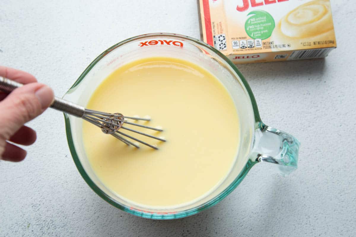 hand whisking pudding in a large glass measuring cup.