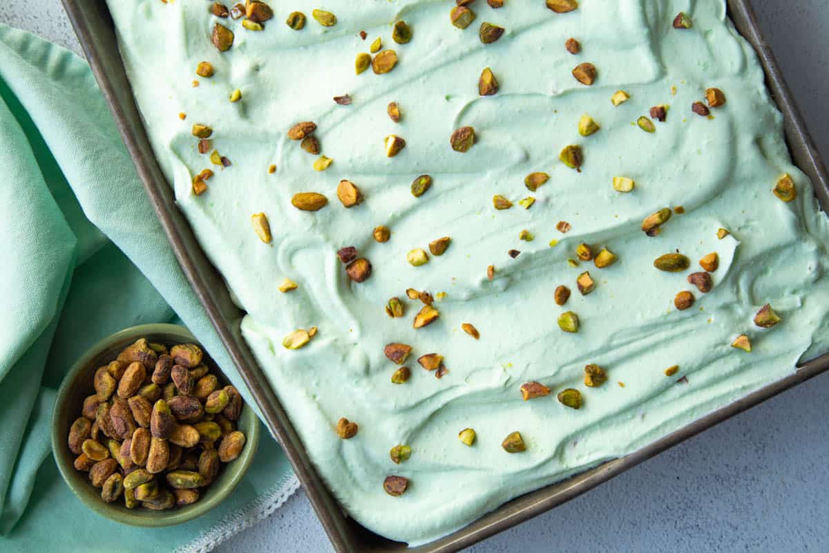 whole pistachio cake topped with green pistachio frosting and chopped pistachios.