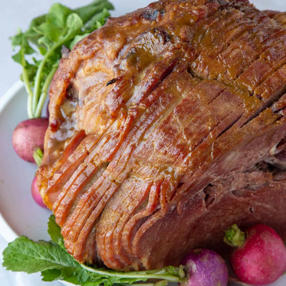 spiral sliced glazed ham on a white platter with pink and purple radishes.