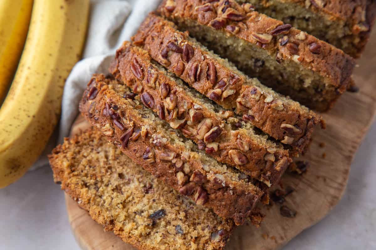 slices of banana bread topped with pecans on a wooden serving board.