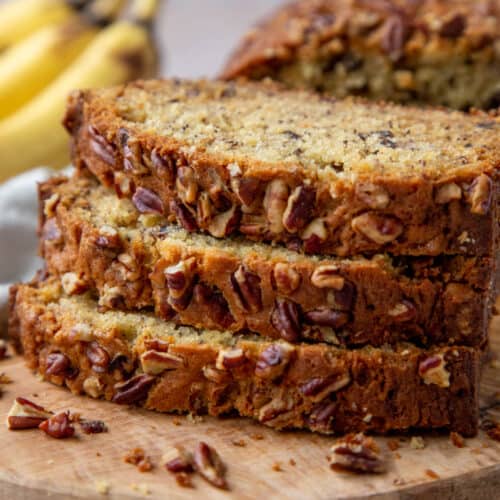 three slices of banana bread with pecans stacked on top of each other on a wooden board.