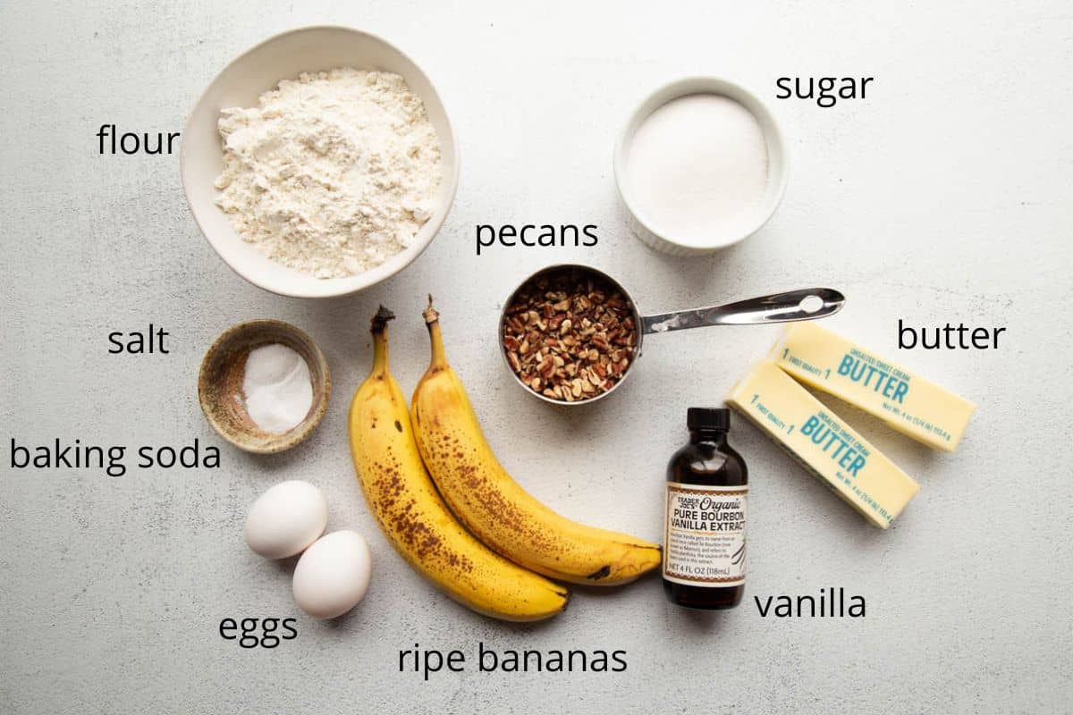 ripe bananas, flour, sugar, butter, and other ingredients on a white table.