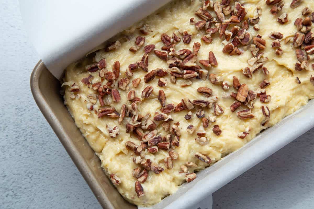 banana bread batter in a parchment lined loaf pan, topped with chopped pecans.