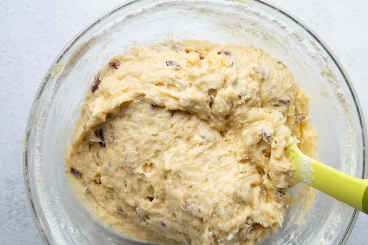 banana bread batter with pecans in a glass bowl with a yellow spatula.