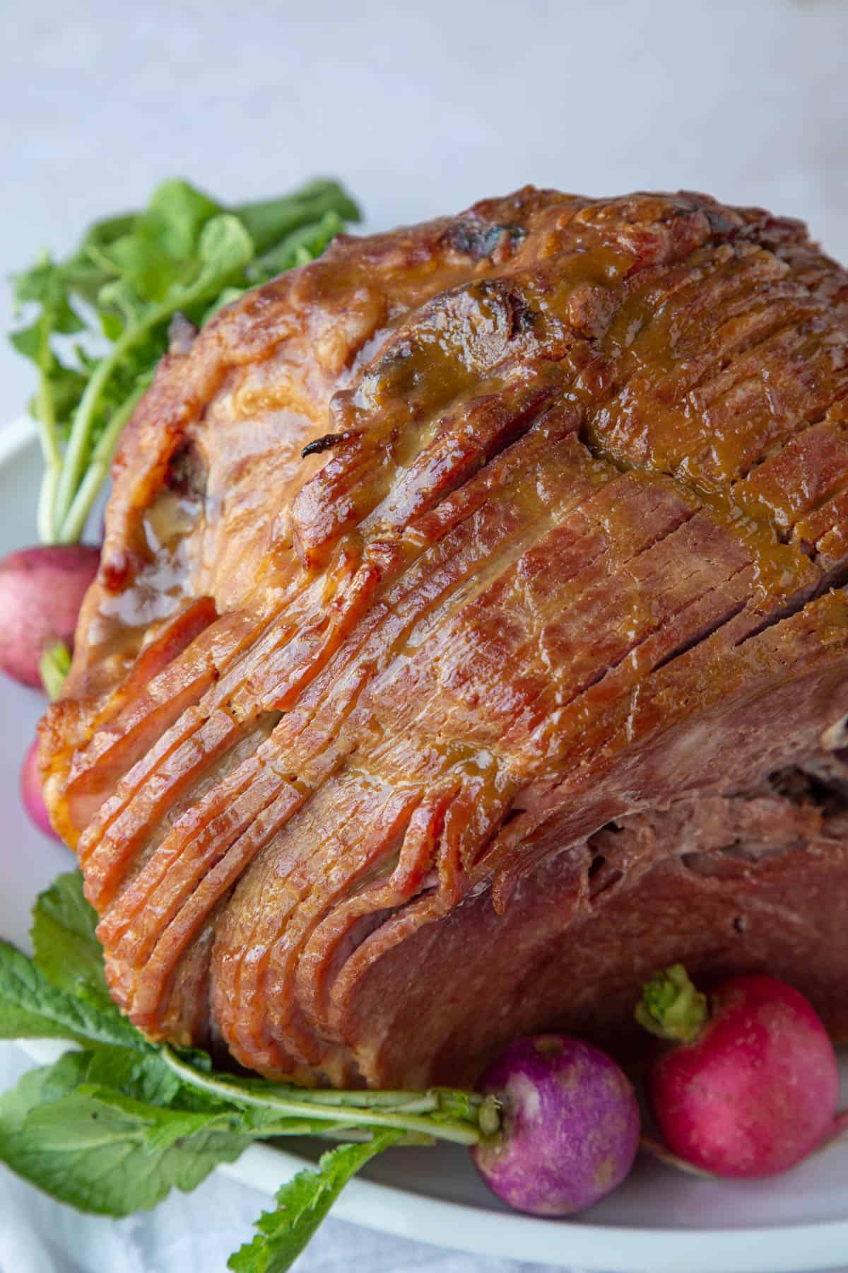 brown sugar glazed spiral sliced ham on a white platter with colorful radishes.