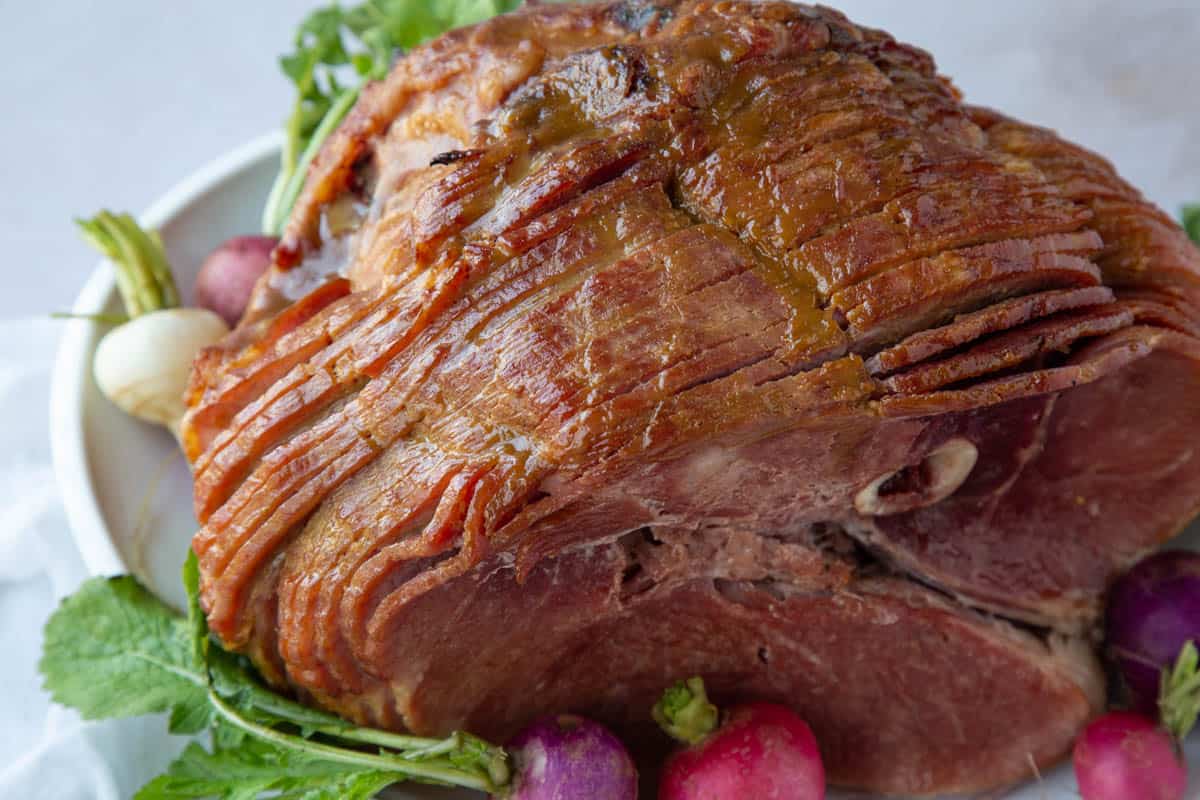 brown sugar glazed ham on a platter with red and pink radishes.