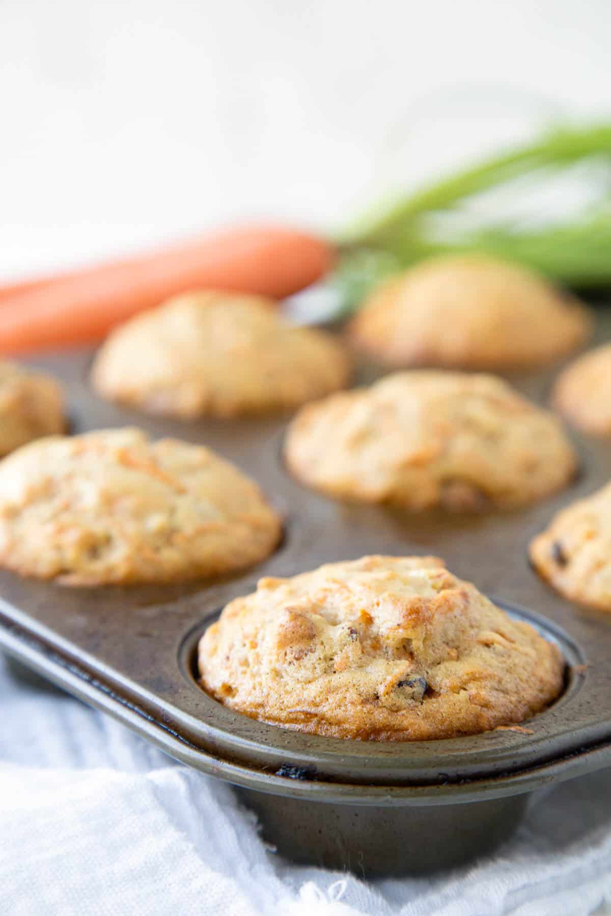 carrot muffins in a metal muffin tin next to whole carrots.