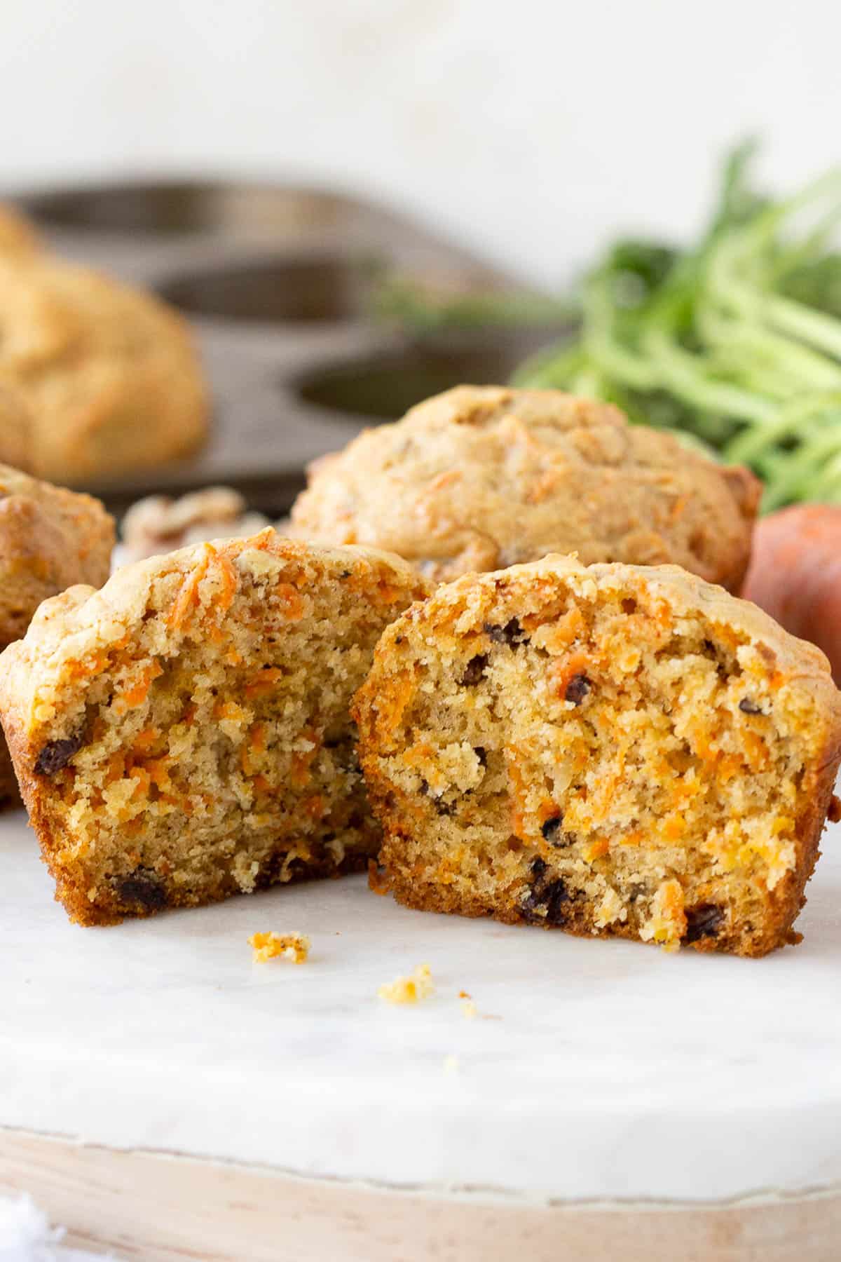 carrot muffin with walnuts and raisins cut in half on a white marble platter.