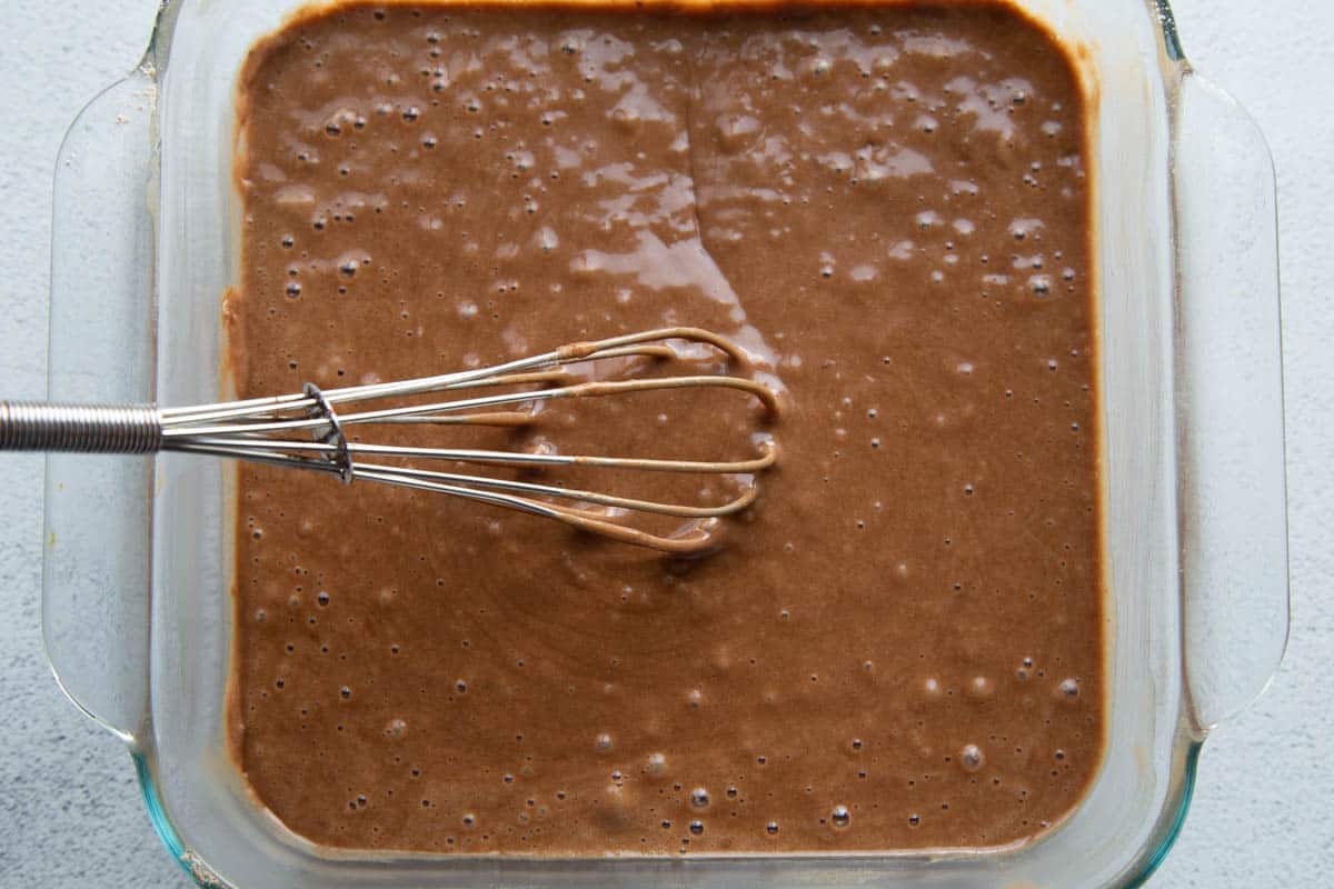 chocolate cake batter in a square glass disk with a whisk.