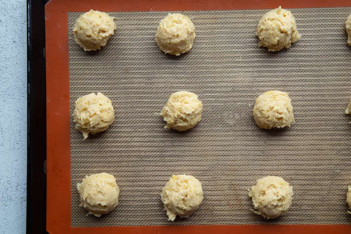 balls of pineapple cookie dough on a baking sheet lined with a silicone mat.