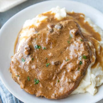 cube steak with gravy on a bed of mashed potatoes on a white plate.