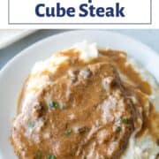crockpot cube steak with gravy on a bed of mashed potatoes on a white plate.