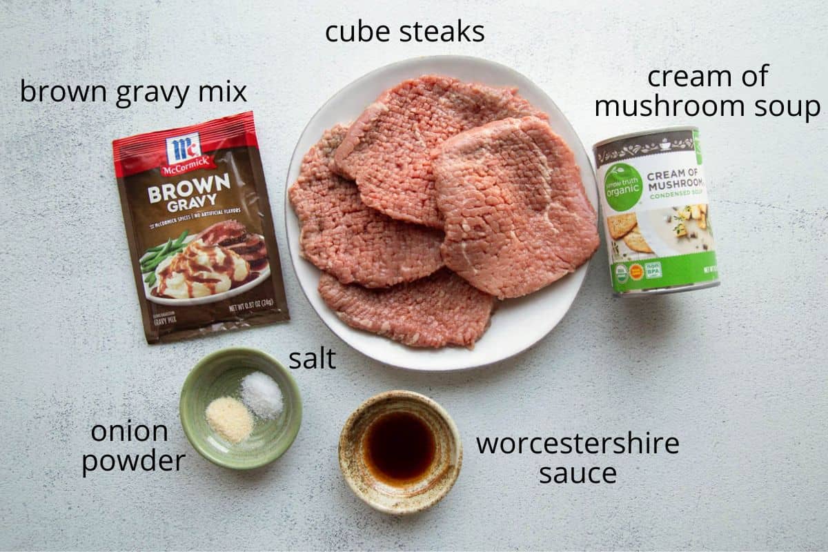 cube steaks, cream of mushroom soup, brown gravy mix, and other ingredients on a white table.
