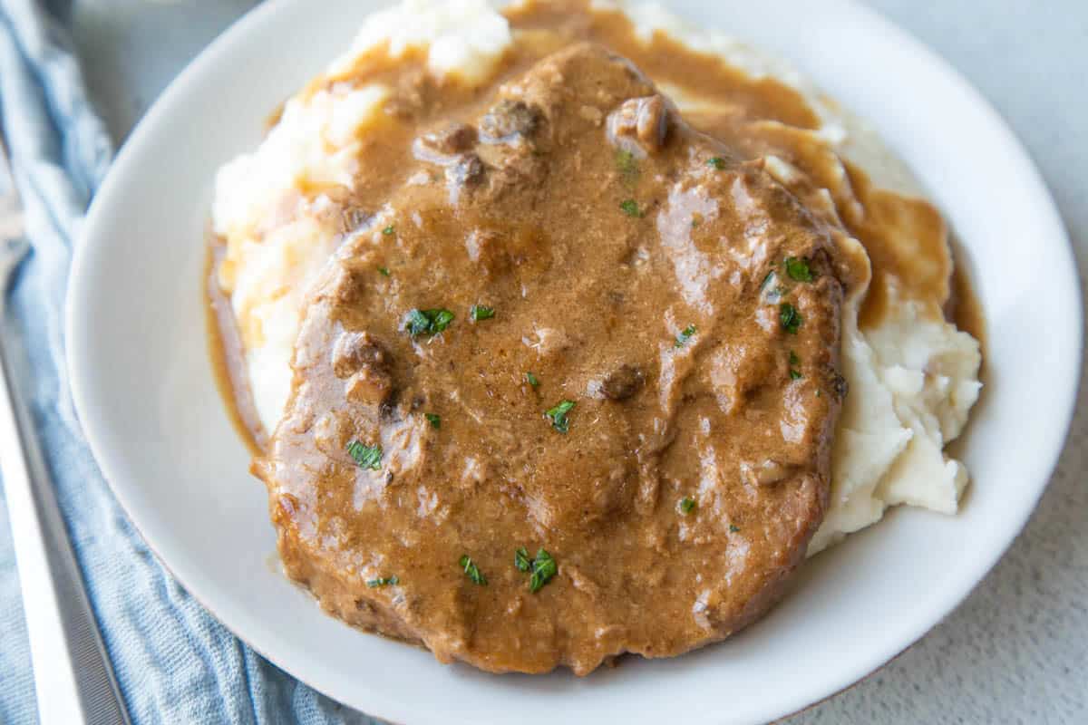 cube steak topped with brown gravy on mashed potatoes on a white plate.