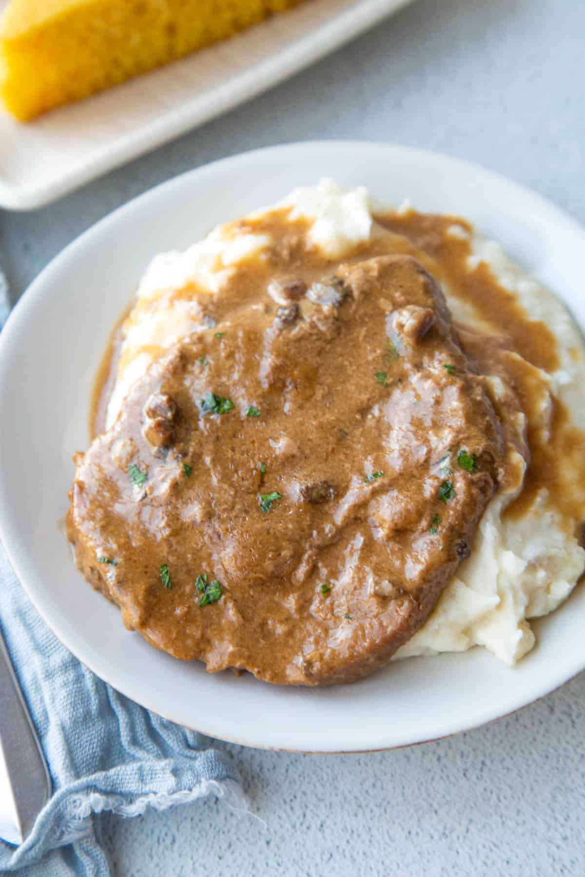 crockpot cube steak with gravy on a bed of mashed potatoes on a white plate.