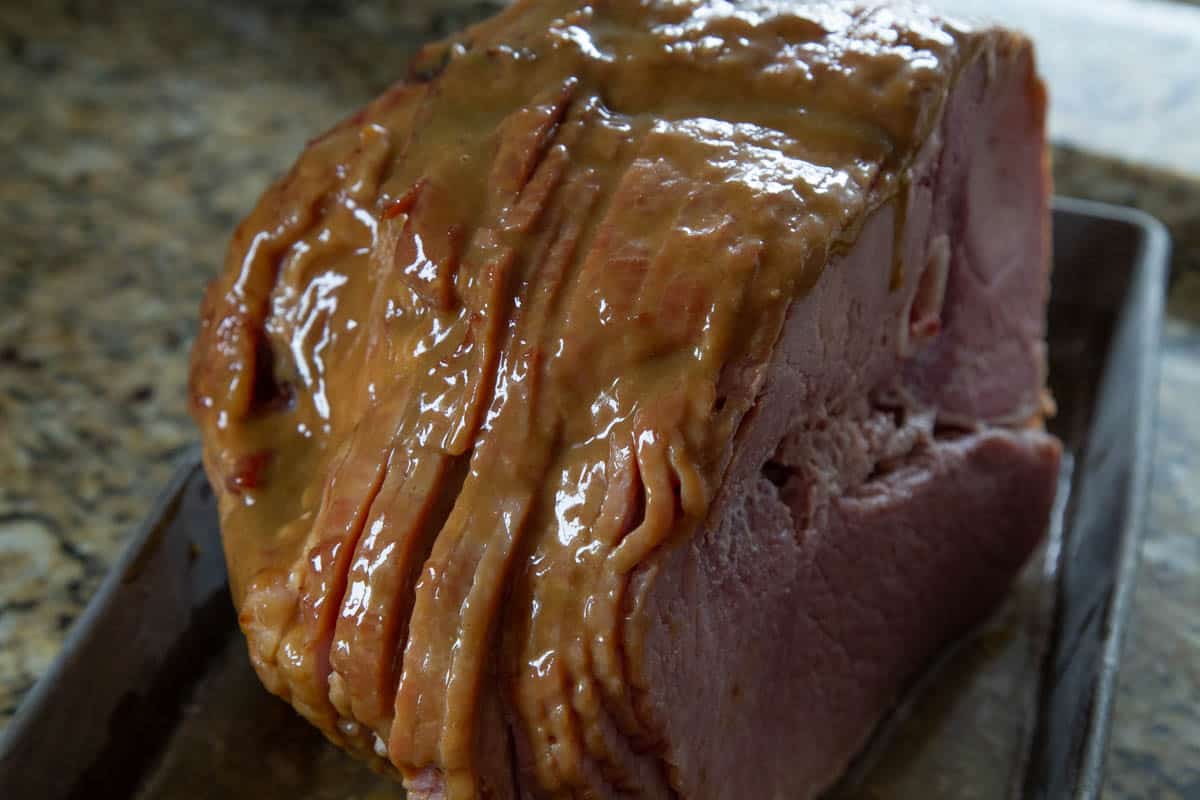 uncooked ham with a shiny glaze in a metal roasting pan.