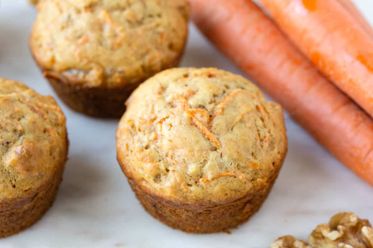 carrot muffins on a white marble platter next to whole carrots.