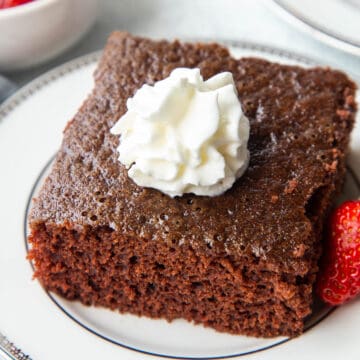 slice of chocolate wacky cake on a white plate, topped with whipped cream.