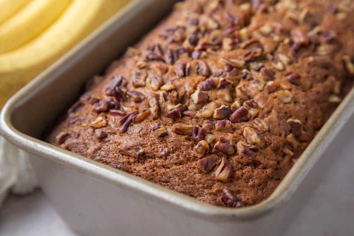 baked loaf of banana bread topped with pecans in a loaf pan.