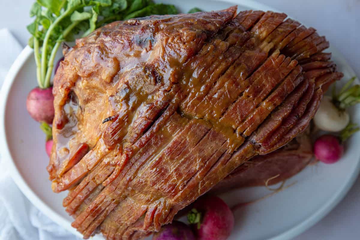 spiral sliced brown sugar glazed ham on a white platter with red and pink radishes.