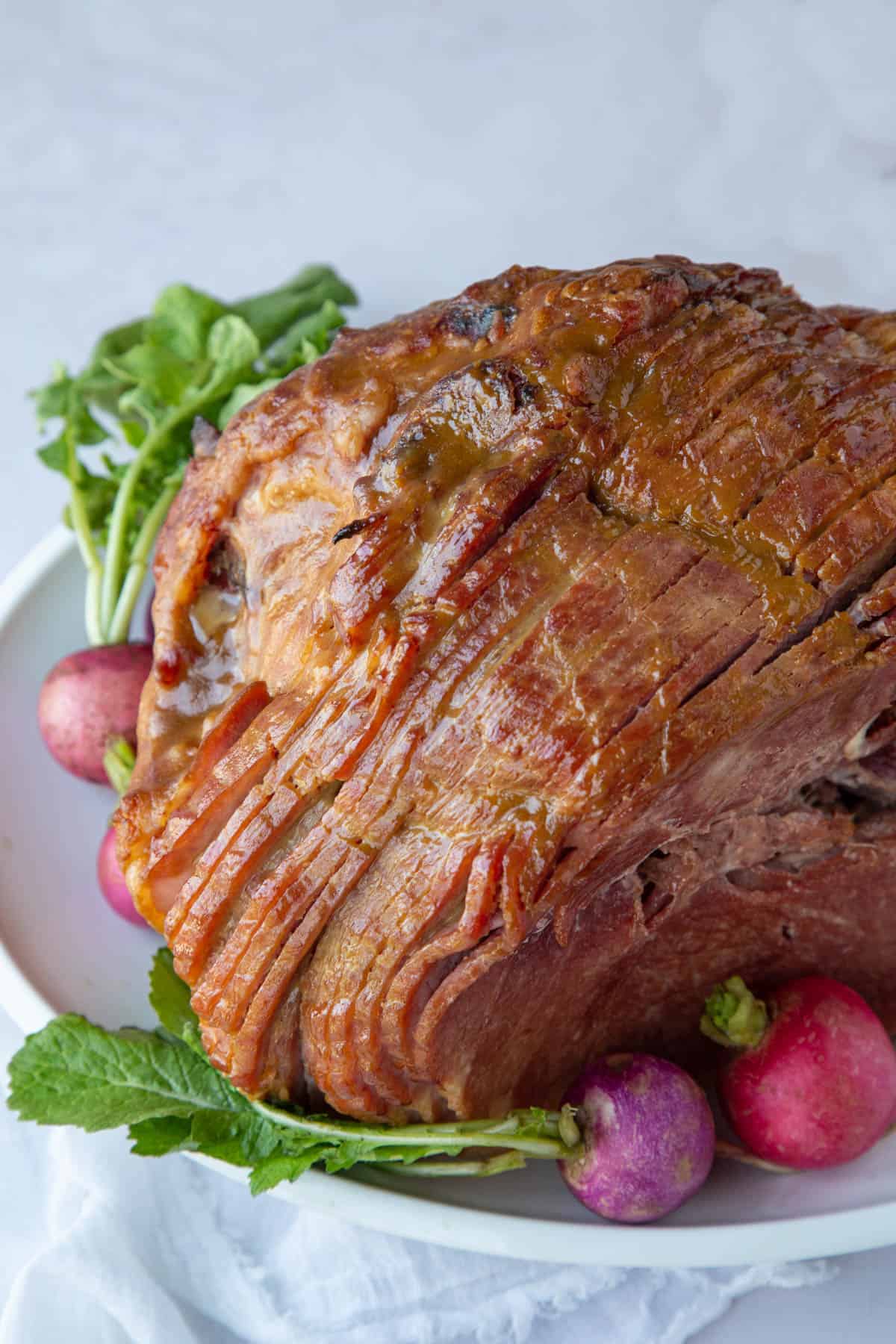 glazed spiral sliced ham on a platter with pink and purple radishes.