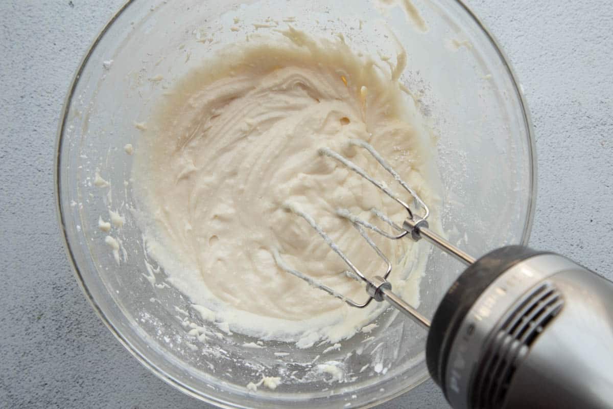 vanilla frosting in a glass bowl with a hand mixer.