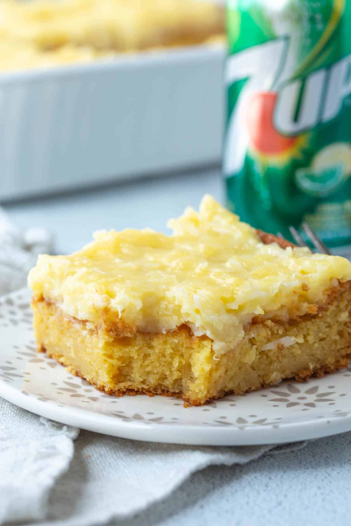 slice of 7up cake topped with coconut pineapple frosting next to a can of 7up.