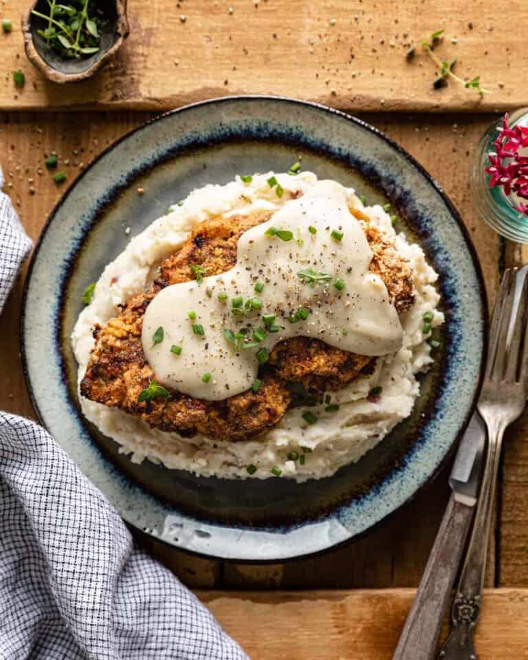 chicken fried steak with white gravy on a bed of mashed potatoes.