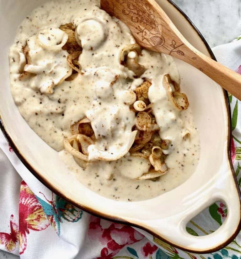 oval casserole dish filled with chicken fried steak and sliced onions in a creamy white gravy.