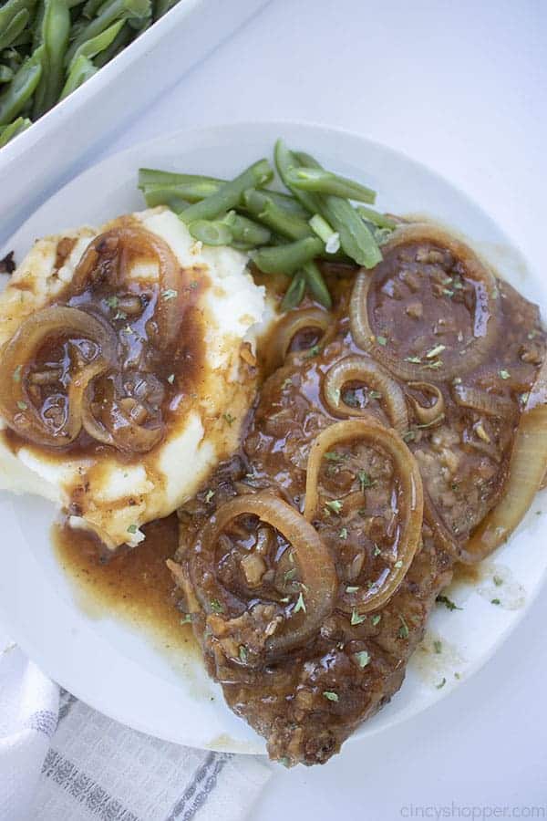 cube steak topped with onions and brown gravy next to mashed potatoes.