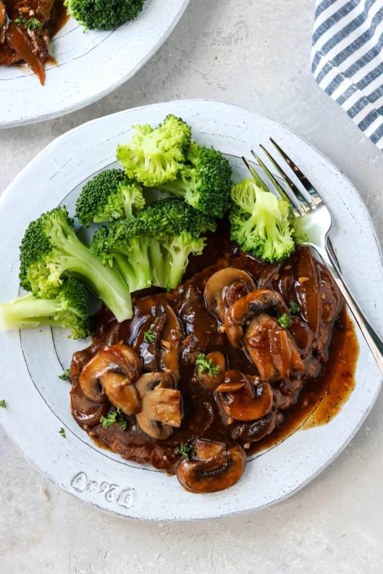 cube steak covered in brown gravy next to a pile of steamed broccoli.
