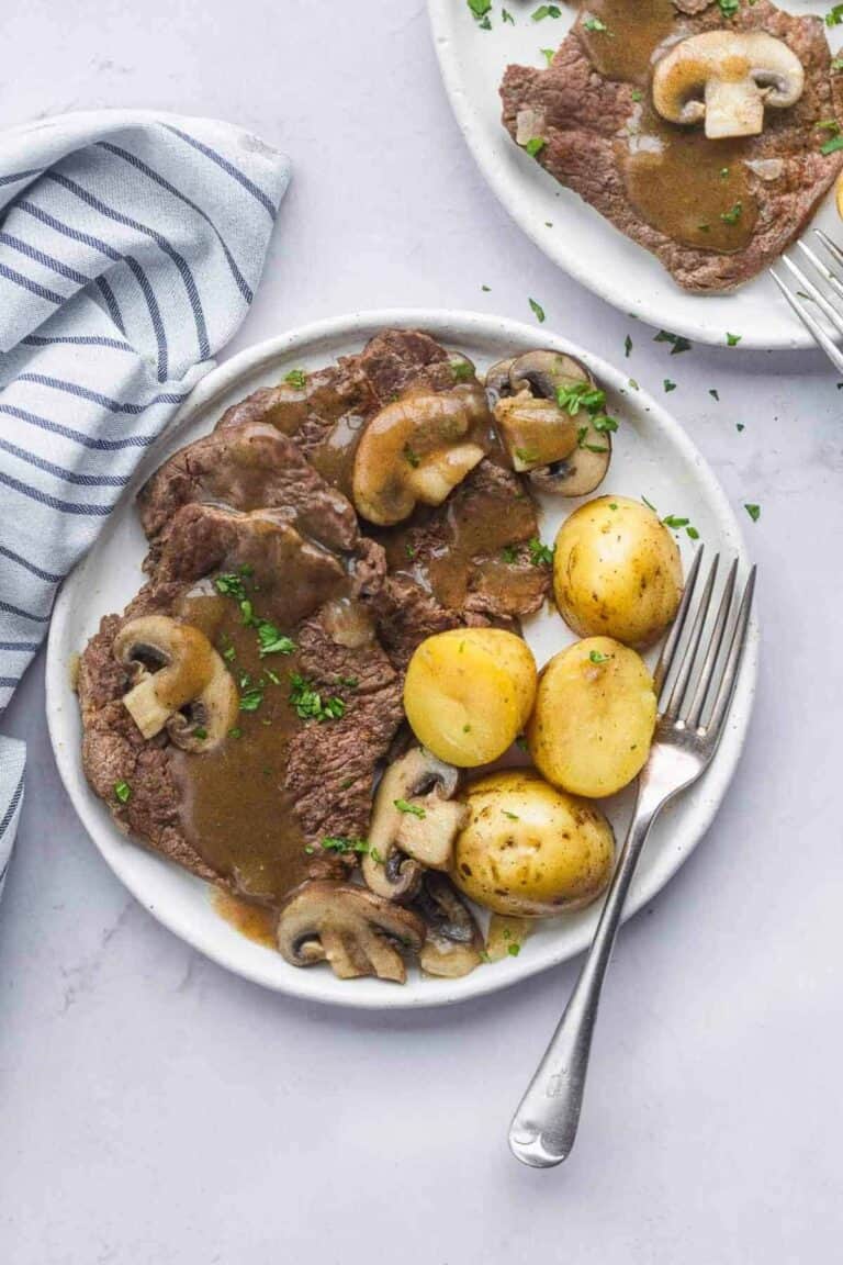 cube steak with potatoes, mushrooms, and onions in a brown gravy on a white plate.